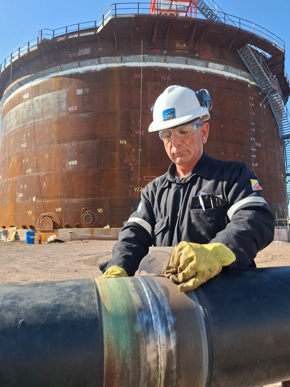Técnico inspeccionando tubería en instalación industrial con tanque